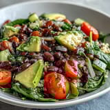 Hearty bowl of mixed beans, quinoa, and sliced avocado topped with zesty lemon dressing. 
