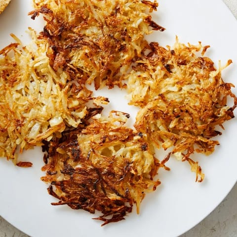 Golden brown, crispy shredded hash browns with a savory onion aroma, fried to perfection in a skillet for a hearty breakfast.