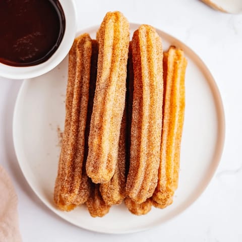 Golden-brown churros with a crispy exterior and soft interior, served warm on a rustic wooden table. 