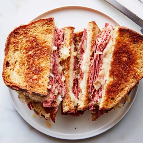 Golden-brown Reuben sandwich sliced in half, revealing layers of corned beef, Swiss cheese, and sauerkraut on toasted rye.