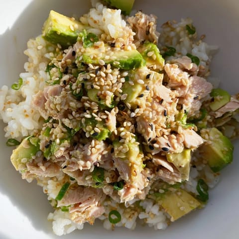 A vibrant Tuna Avocado Rice Bowl with diced avocado, cucumber, and scallions drizzled with a savory sesame-ginger dressing.