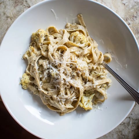 Golden roasted cauliflower alfredo pasta served in a white bowl with a fork on the side.  