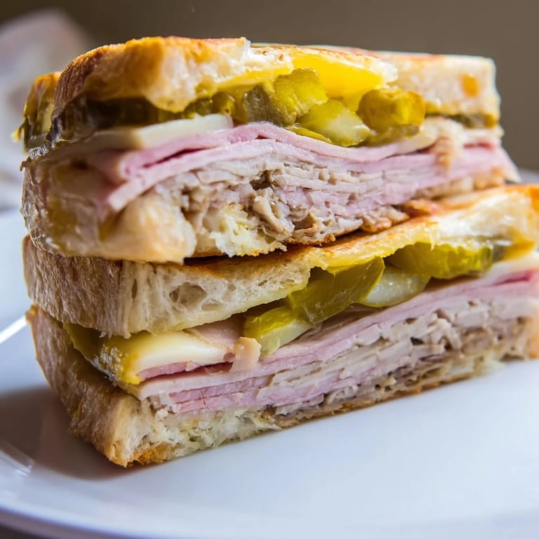 Sliced diagonally to reveal savory layers of pork, ham, and pickles on a classic Cuban sandwich.