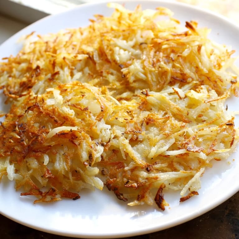 Homemade hash browns, pan-fried to crispy perfection, served alongside fluffy scrambled eggs for a classic American breakfast or brunch.