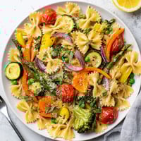 Bright, colorful bow-tie pasta primavera is tossed with fresh spring vegetables like asparagus and cherry tomatoes in a light garlic lemon sauce.