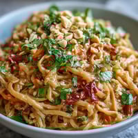 Asian Peanut Noodle Bowl with crunchy vegetables and creamy peanut dressing in a white bowl, topped with peanuts and lime wedges.
