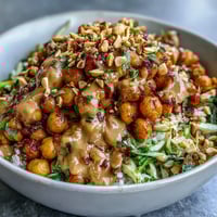 Roasted chickpeas and crisp veggies sit atop brown rice in a vibrant Peanut Chickpea Protein Bowl, drizzled with creamy peanut sauce.